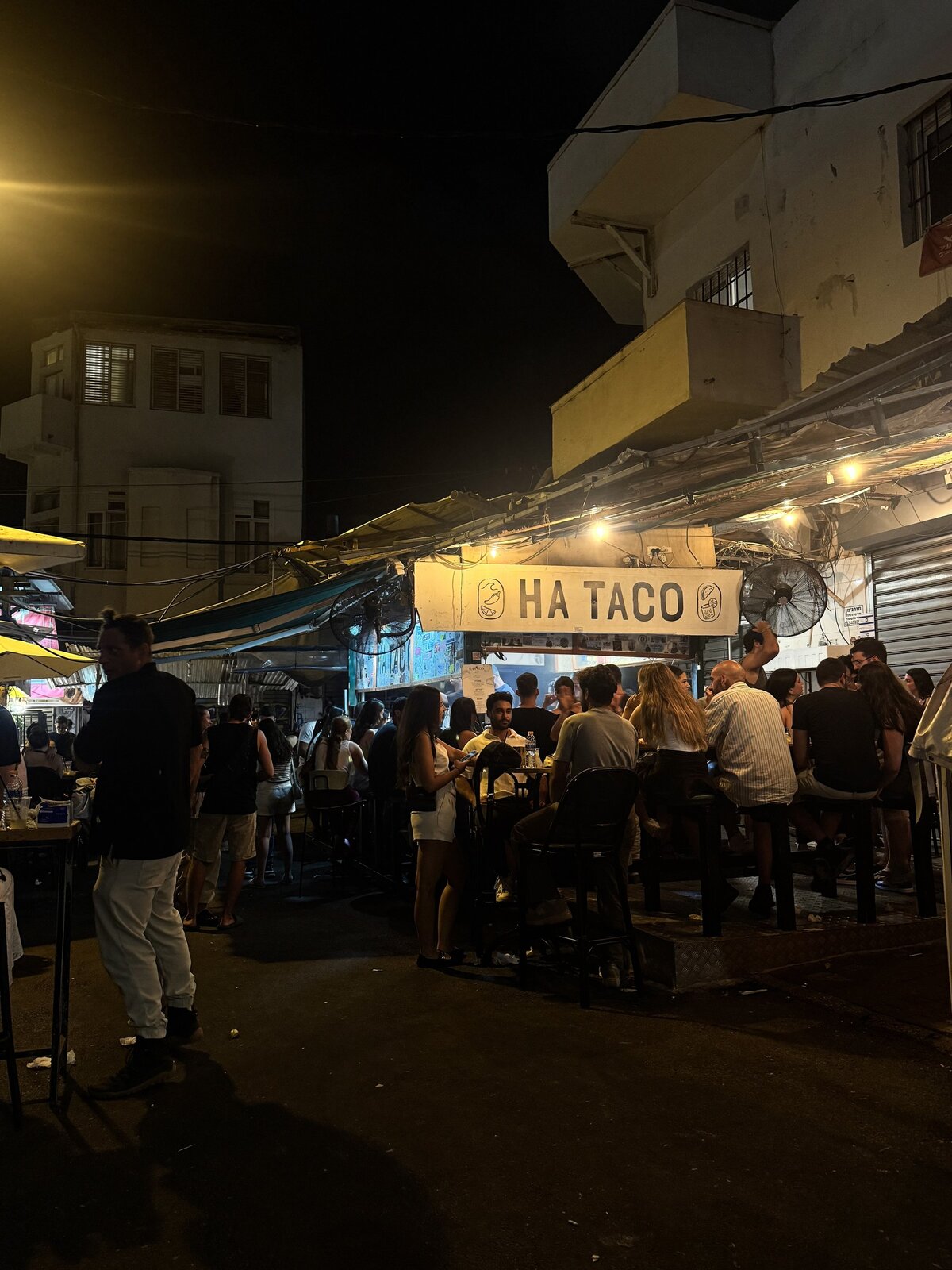 HA TACO stall lit at night with a crowd in Carmel Market
