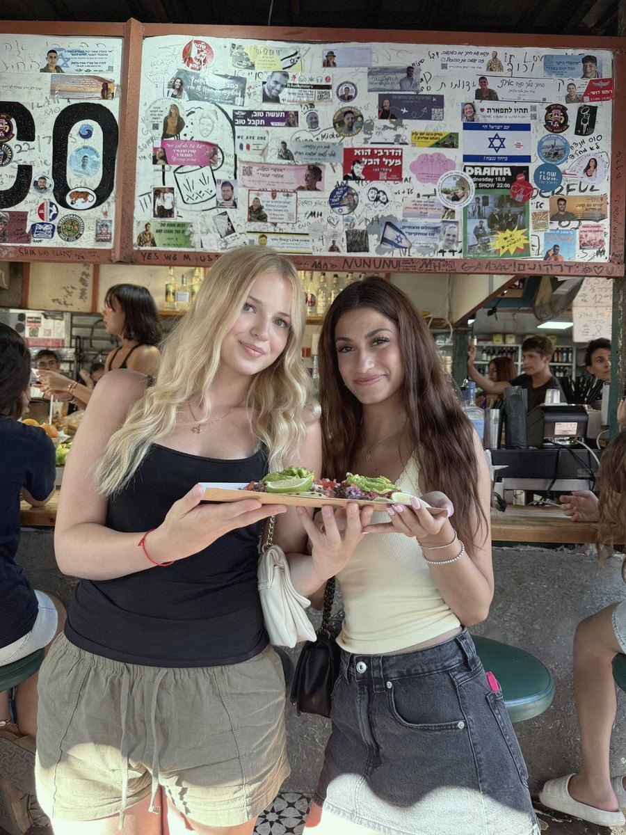 שתי חברות עם מגש טאקו מתחת לשלט